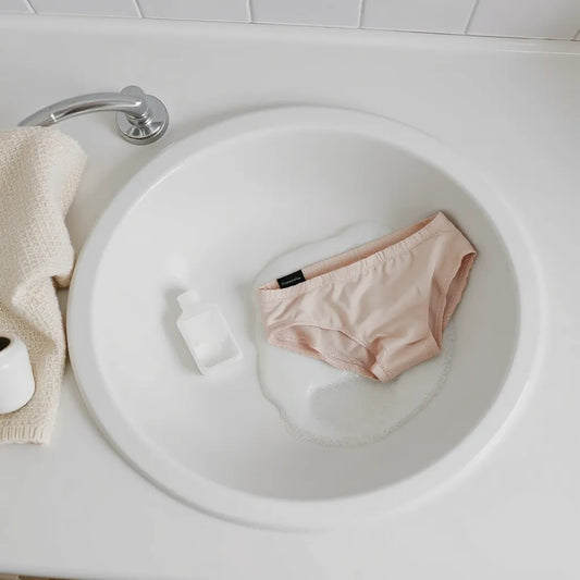 Detergent and period underwear prepared for a gentle wash in a clean laundry setting.